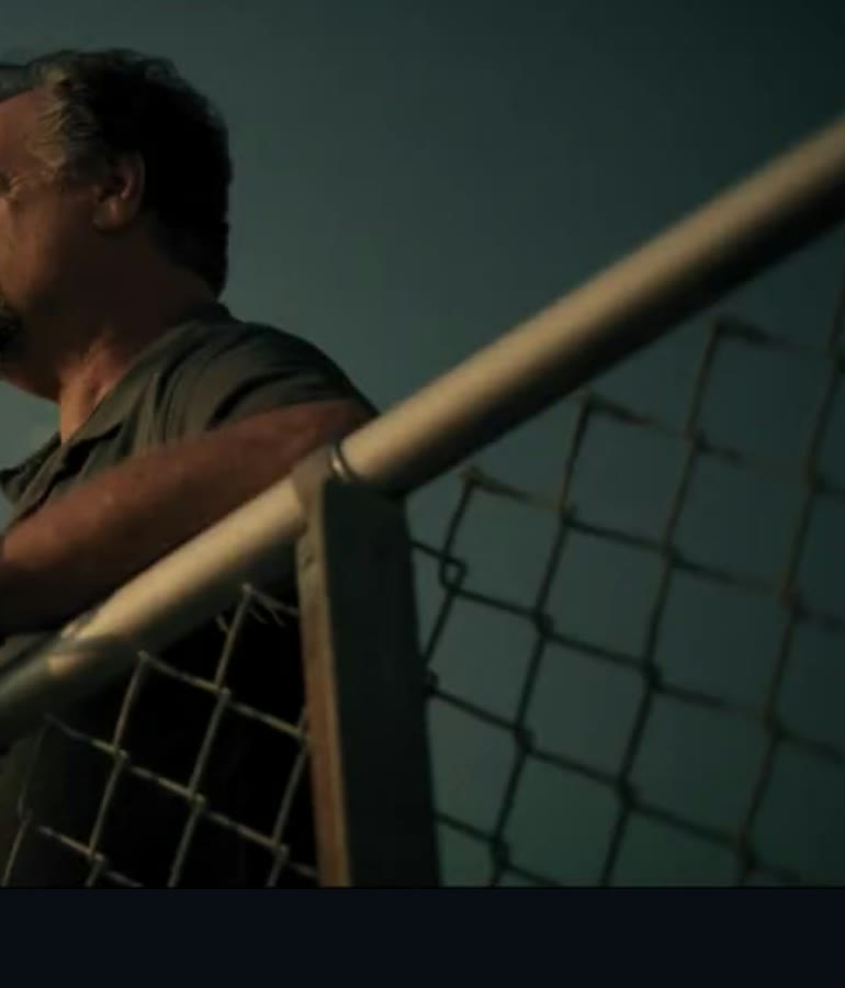 The finished comp. The real man leaning on the bleacher rail in warm light, sitting inside the AI-assisted wide, reading as one continuous shot.